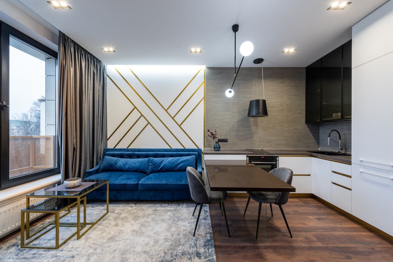 services-06 Interior of modern apartment with blue sofa on carpet near window with curtain near table with chairs near kitchen with counter and cabinet with stove and oven near sink
