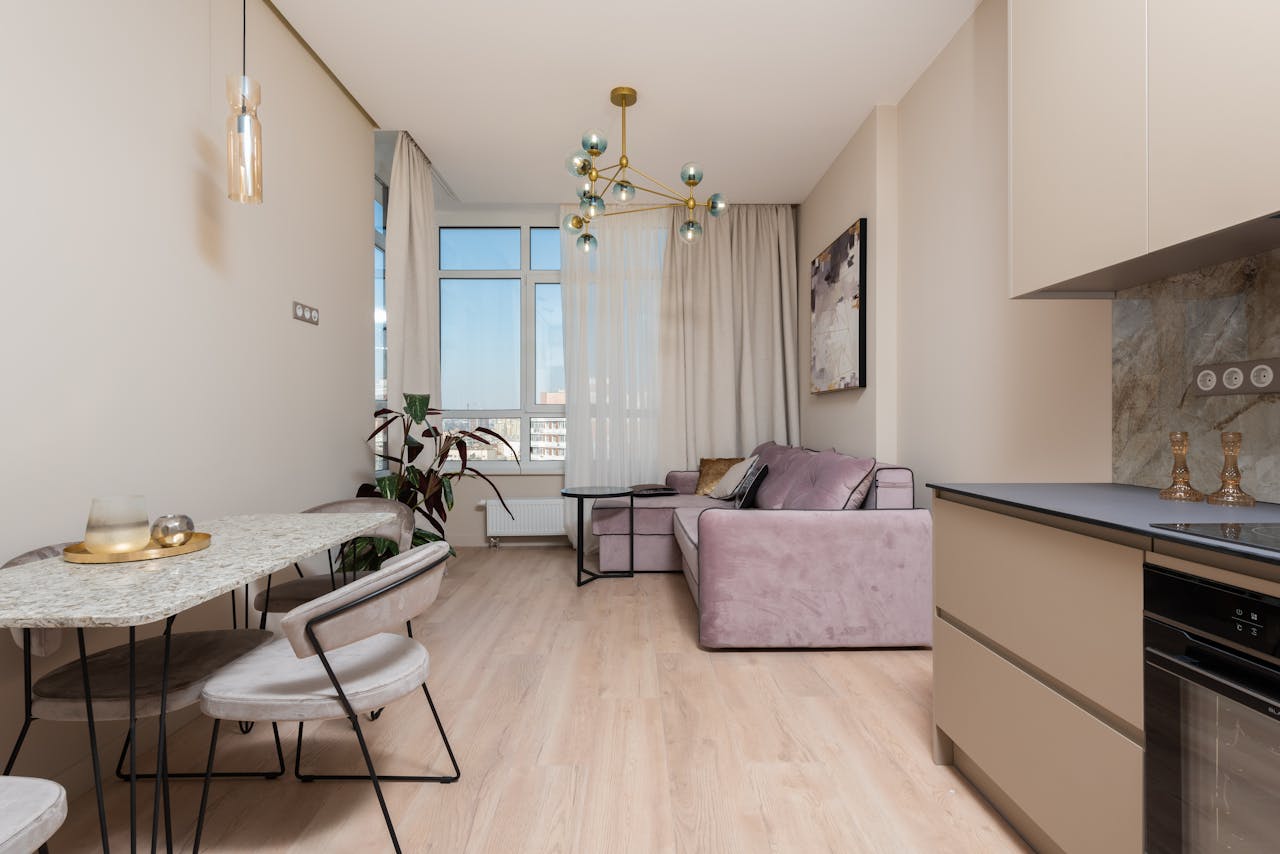 about-us Interior of bright modern studio with open kitchen with cabinets near table and chairs next to couch with pillows near window with curtains